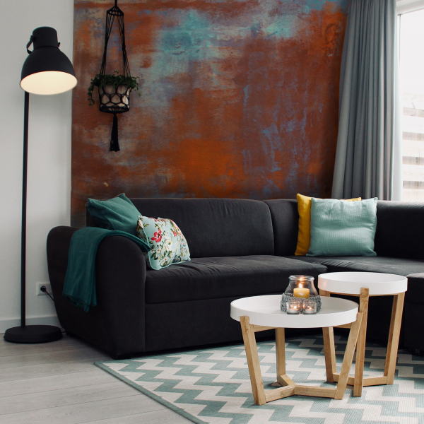 Modernes Wohnzimmer mit Akzentwand in Rost- und Kalk-Optik, dunklem Ecksofa, bunten Kissen und weißen Beistelltischen auf geometrischem Teppich